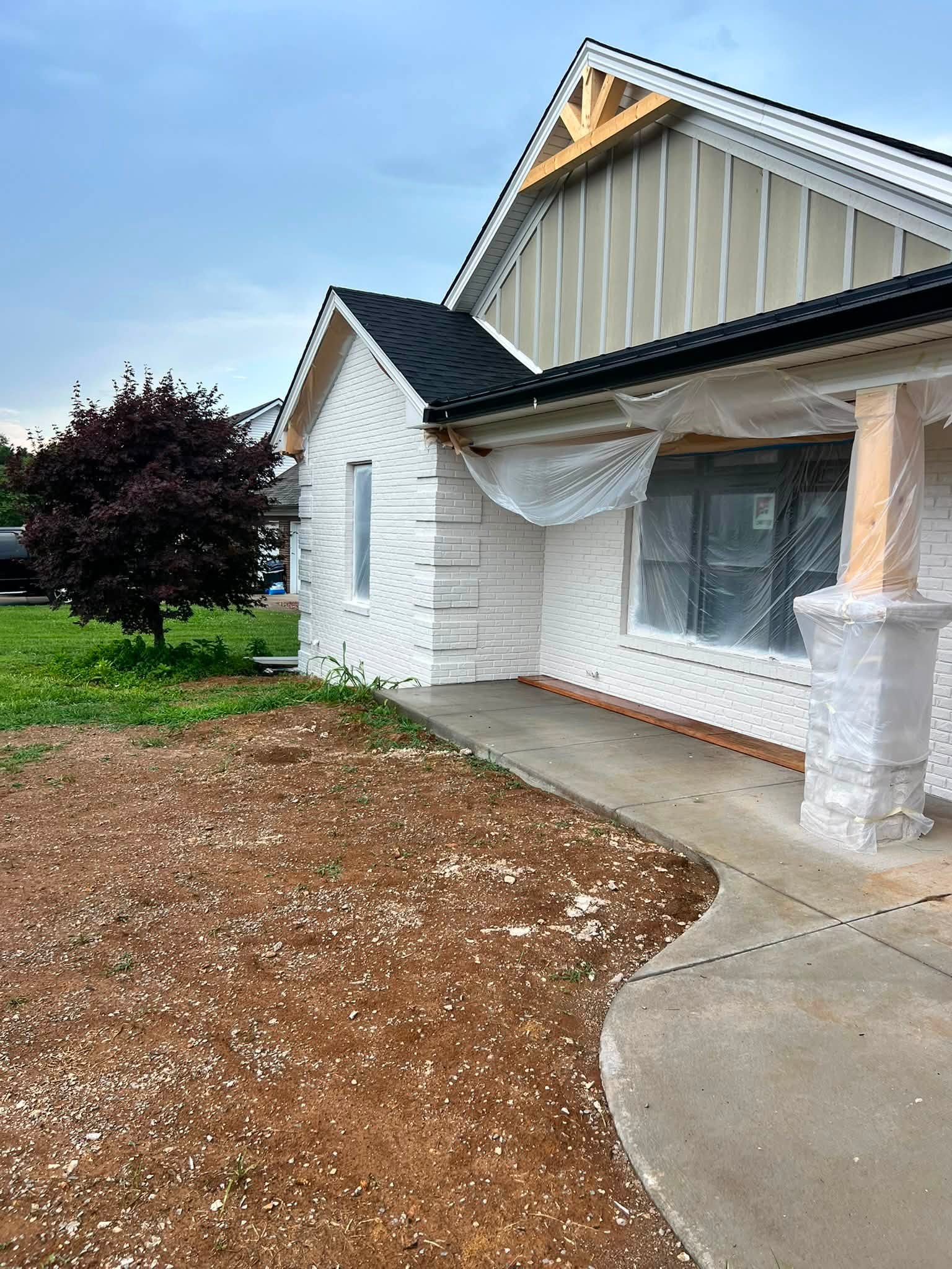 A house under renovation with freshly white-painted brick, exposed roof gable framing and plastic-wrapped windows and columns.