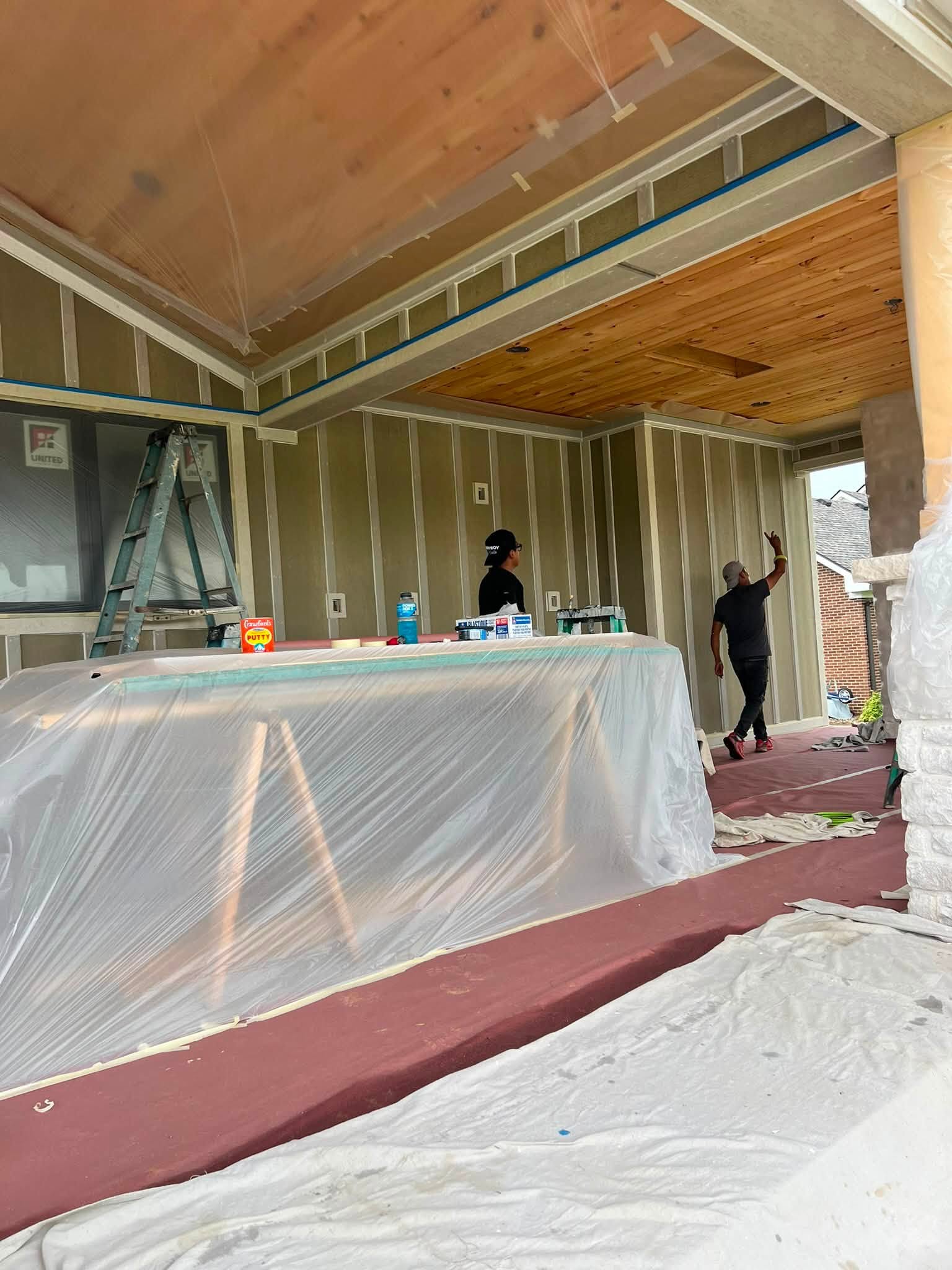 Two crew members installing a tongue-and-groove wood ceiling on a new covered outdoor living space, seen from behind.