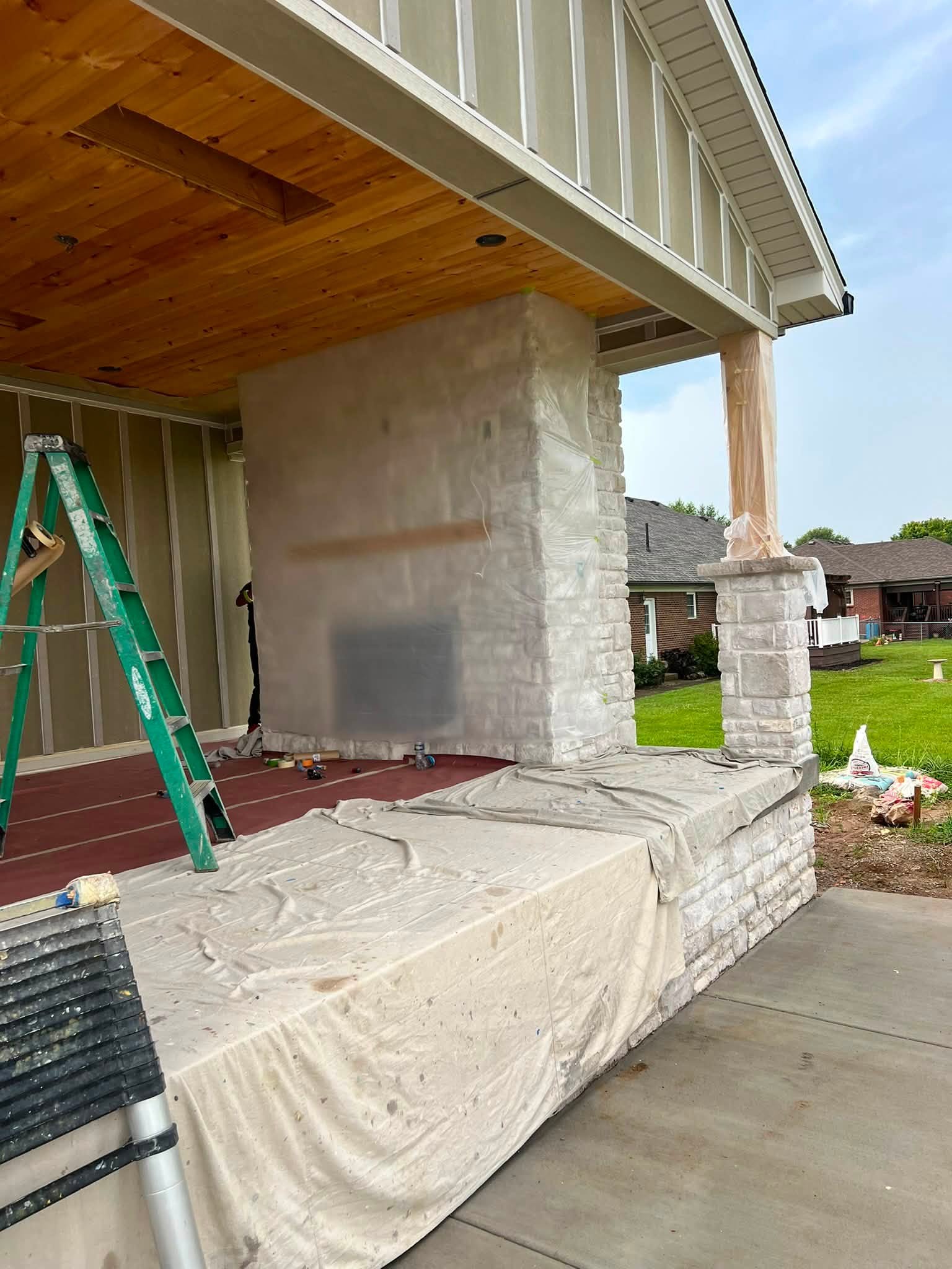 A partly finished outdoor fireplace column faced in stacked stone, wrapped in plastic sheeting during finish work.